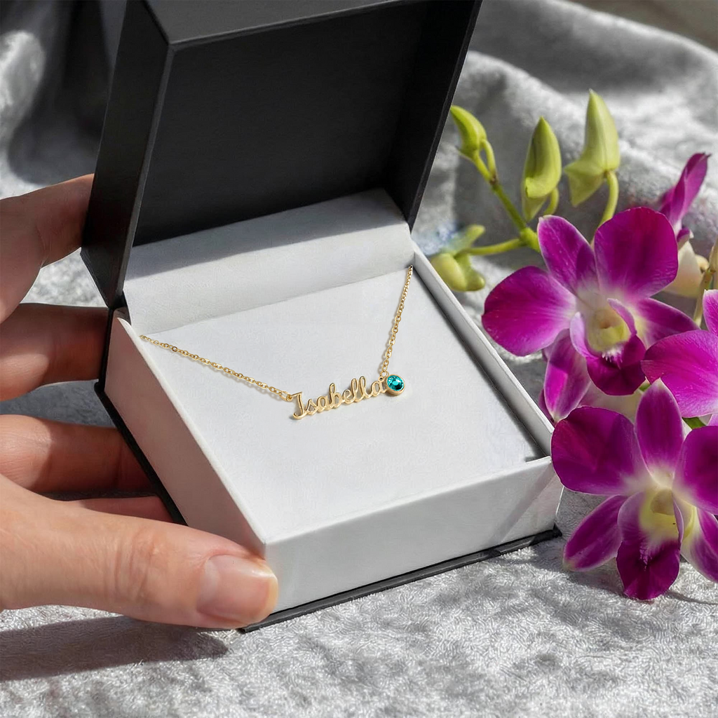 Gold name necklace in open gift box with blue-green round birthstone on chain
