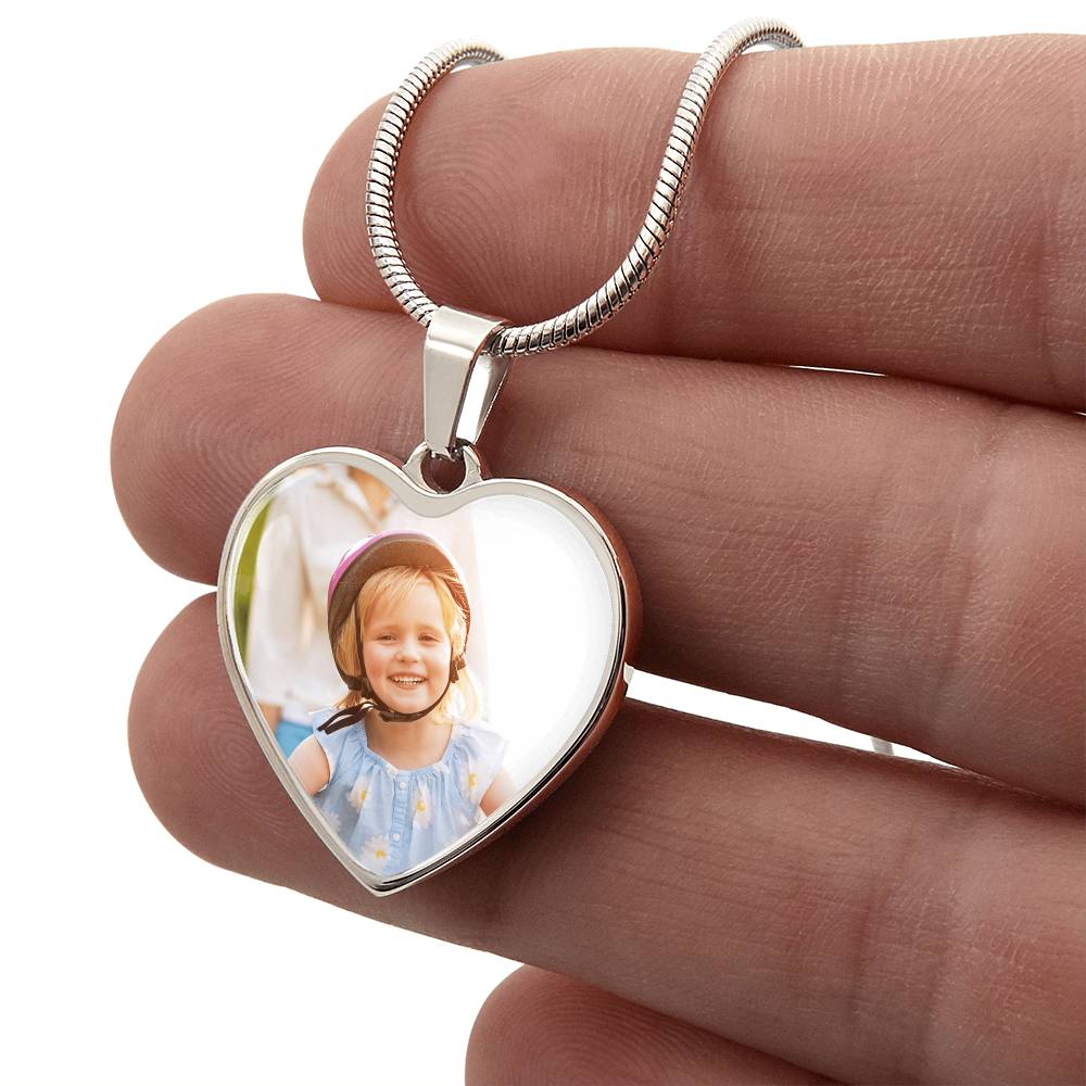 Silver heart photo pendant on chain held in fingers, clear photo window