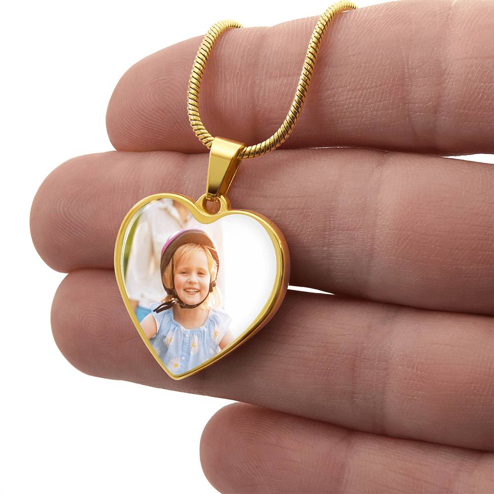 Gold heart photo pendant on chain held in fingers, clear photo window