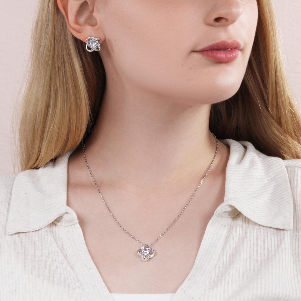 Silver-tone love-knot necklace with heart pendant and small stud earrings on person