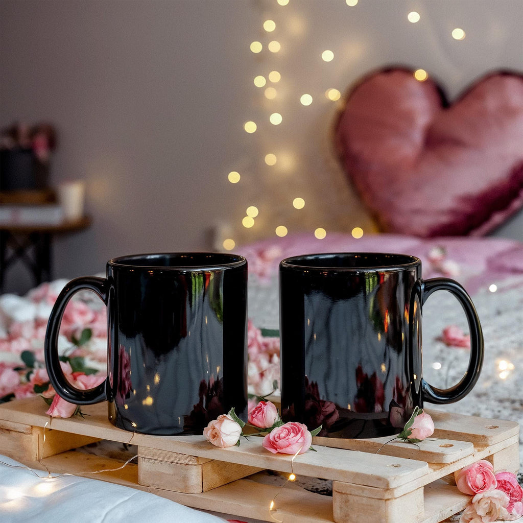 Black glossy ceramic mug pair, side-by-side with decorative flowers nearby
